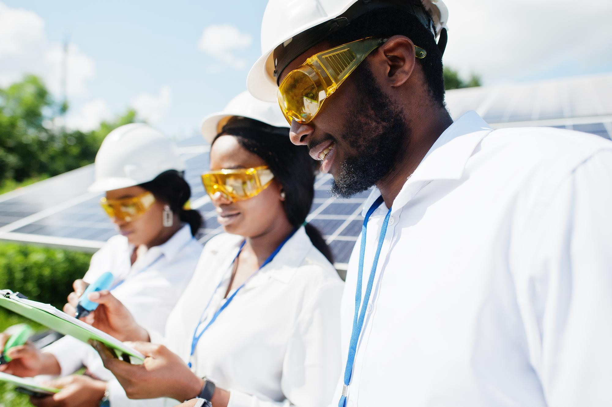 African clean-energy professionals reviewing work near solar panels